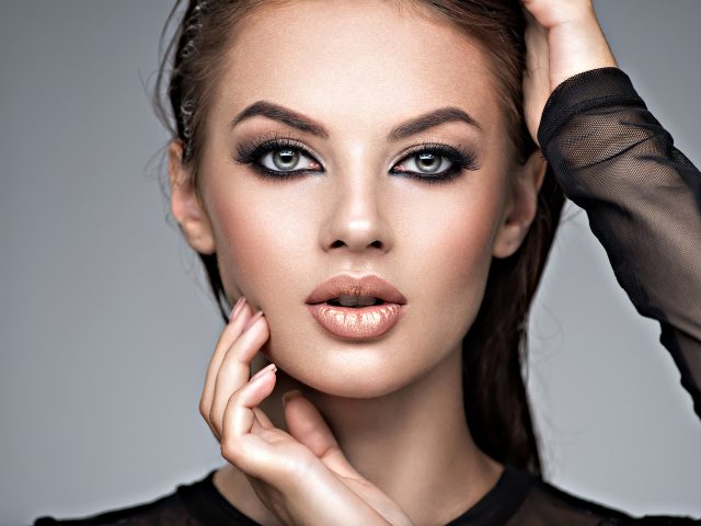 Beauty face of the young beautiful woman. Gorgeous female portrait with slicked brown hair. Young adult girl with healthy skin. Pretty model with fashion smokey eye makeup. Skin care concept. Professional makeup