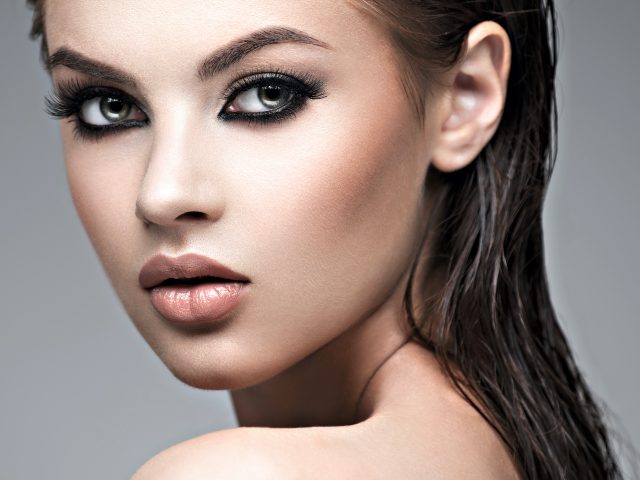 Beauty face of the young beautiful woman. Gorgeous female portrait with slicked brown hair. Young adult girl with healthy skin. Pretty model with fashion smokey eye makeup. Skin care concept. Professional makeup